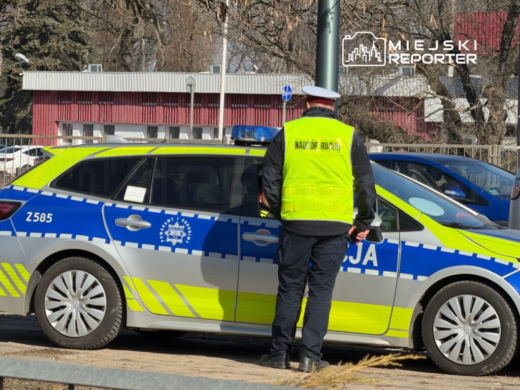 Policjant w kamizelce odblaskowej nadzorujący ruch obok oznakowanego radiowozu na miejskiej ulicy.