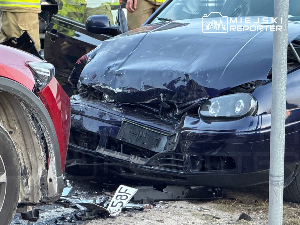 Czarny samochód osobowy z uszkodzoną przednią częścią stoi obok czerwonego auta po wypadku drogowym.