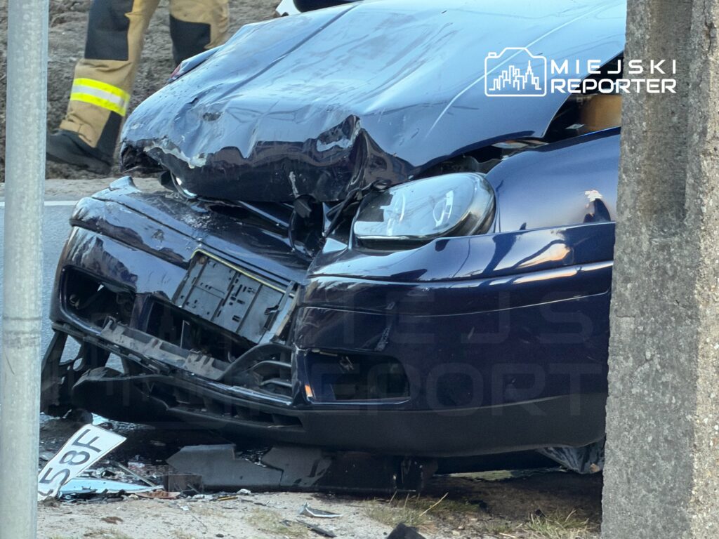 Uszkodzony samochód osobowy leży na poboczu drogi, obok widoczny strażak w mundurze.