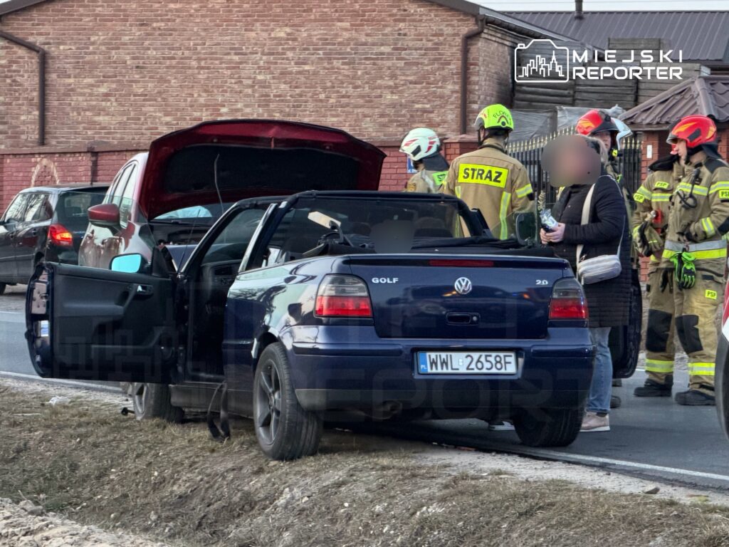 Kobieta rozmawia z ratownikami przy samochodzie osobowym z otwartą maską na poboczu drogi.