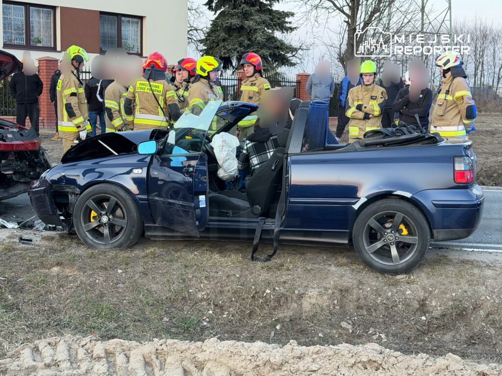 W miejscu wypadku drogowego, strażacy w mundurach omawiają sytuację obok uszkodzonego samochodu kabrioletu.
