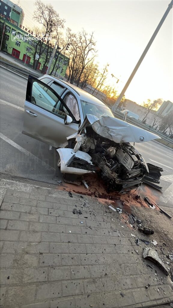 Uszkodzony samochód osobowy z wgniecionym przodem leży na poboczu drogi, obok leżą fragmenty karoserii.