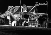 Uszkodzony samochód leży na poboczu drogi, a w tle widać osobę w odzieży ochronnej przy namiocie.