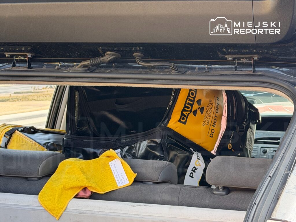 W bagażniku samochodu widoczne są torby z oznaczeniem "Caution: Radioactive Materials" oraz żółta ściereczka.