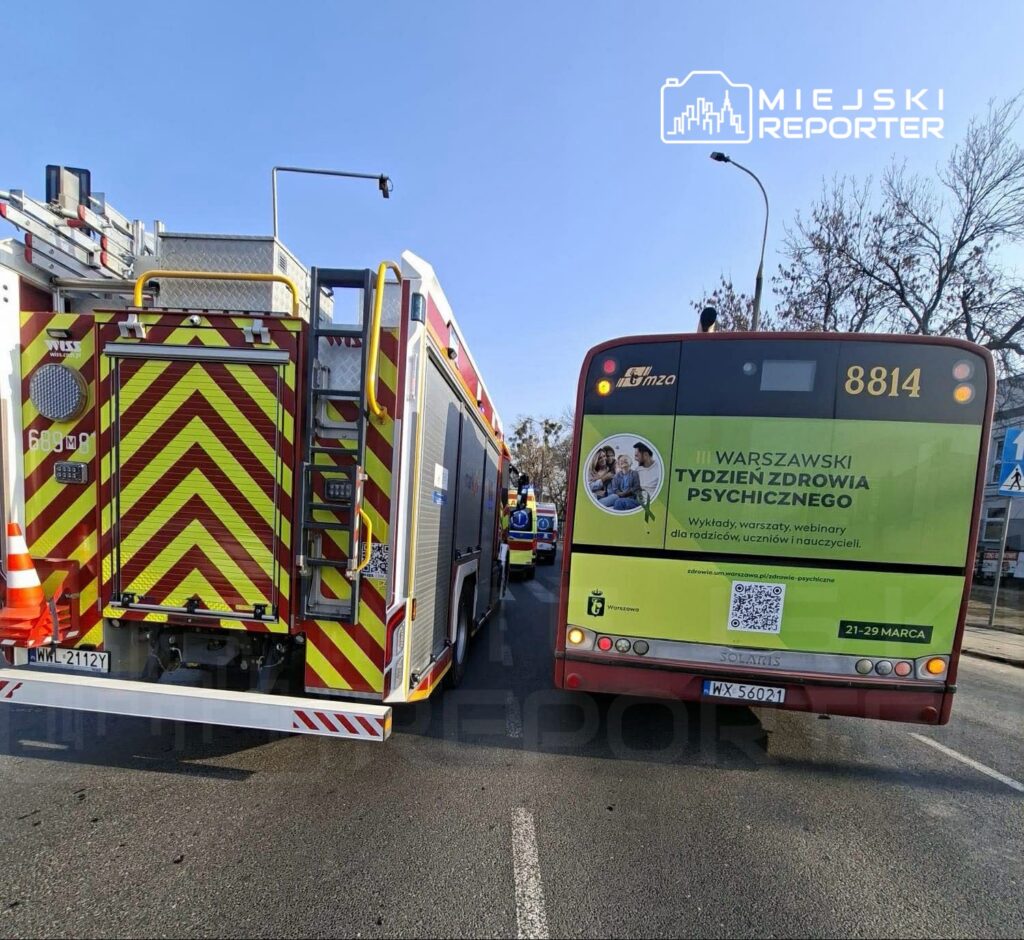 Strażacki wóz z charakterystycznym oznakowaniem stoi na ulicy obok autobusu z reklamą "III WARSZAWSKI TYDZIEŃ ZDROWIA PSYCHICZNEGO".