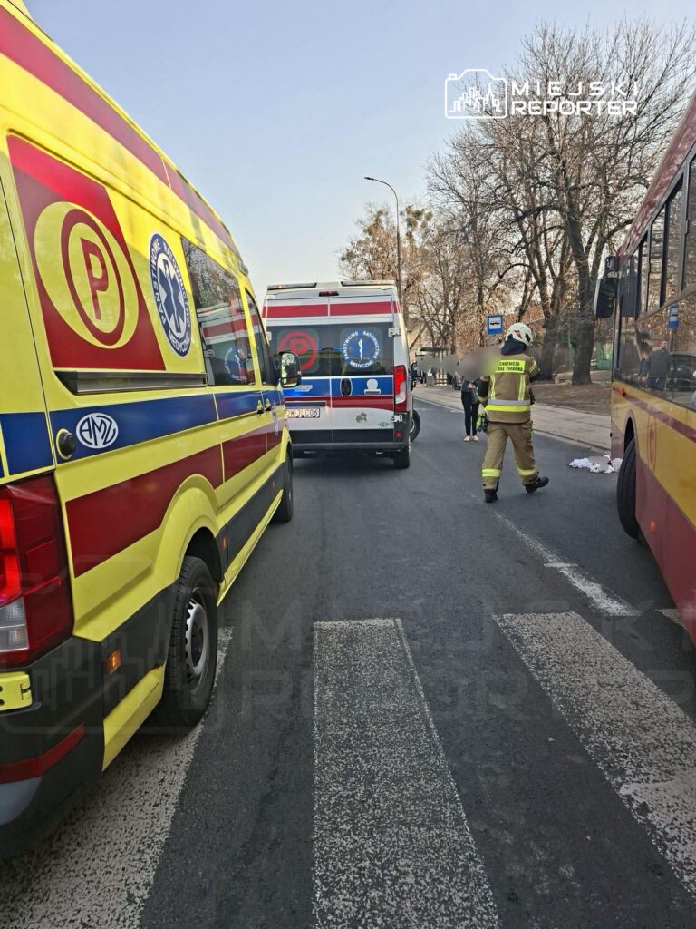 Zespół ratownictwa medycznego i strażacy interweniują na drodze, obok zaparkowanych ambulansów.