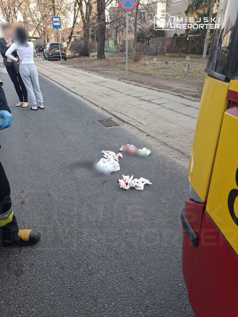Grupa ludzi w pobliżu drogi, jeden z uczestników rozmawia z drugim, na jezdni leżą poszarpane materiały.