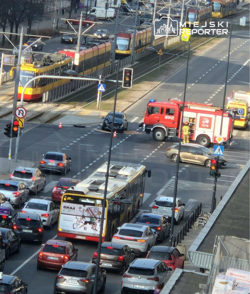 Samochód osobowy zderzył się z innym pojazdem na skrzyżowaniu, a obok stoi wóz strażacki z włączonymi sygnałami.