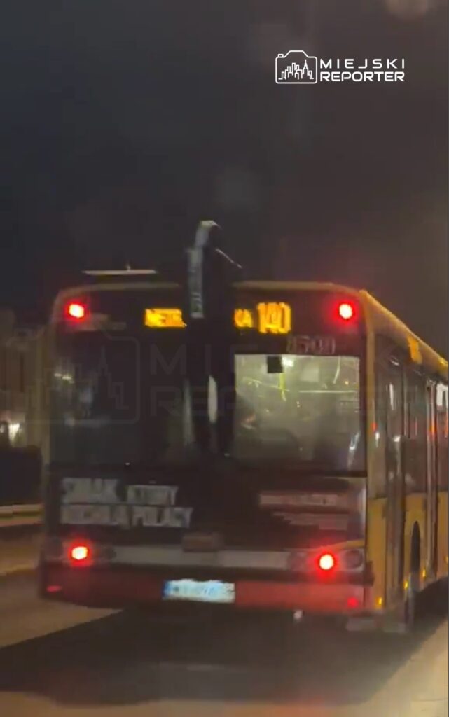Mężczyzna wspinający się na tył autobusu miejskiego podczas nocnej jazdy. Na wyświetlaczu widoczny numer linii 140.