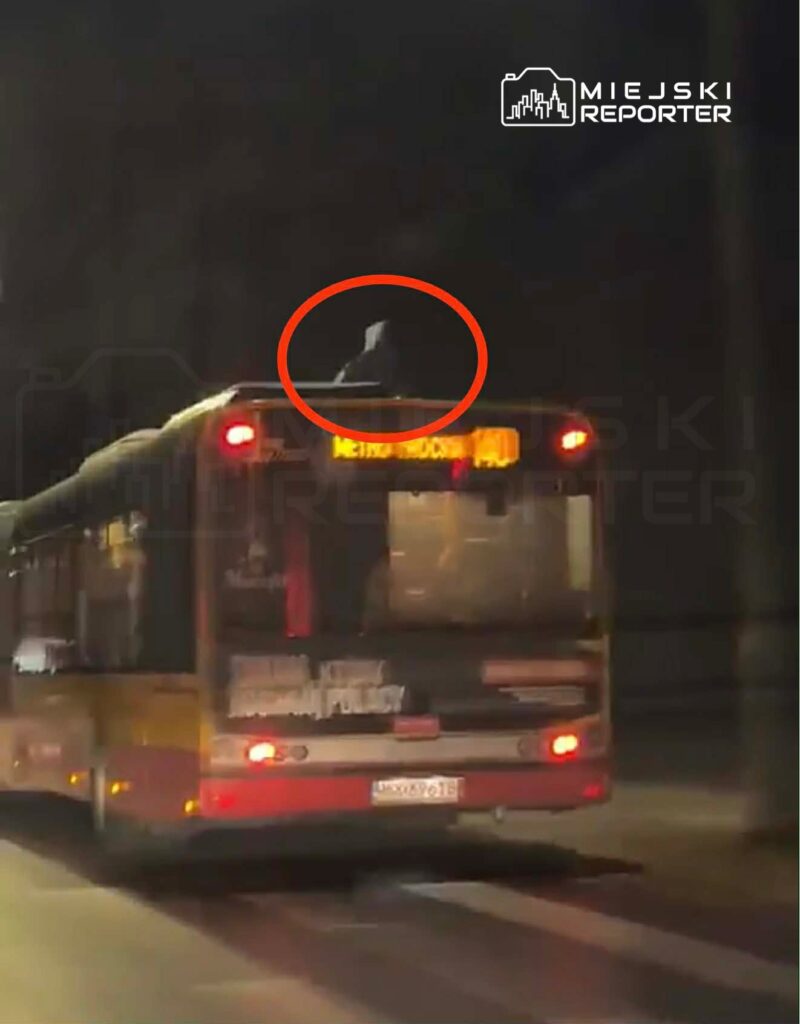 Na dachu autobusu miejskiego widoczna jest sylwetka osoby w ciemnym ubraniu, jadącego nocą ulicą.
