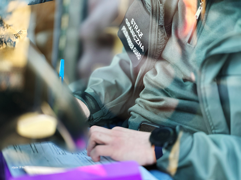 Funkcjonariusz Straży Granicznej w mundurze zapisuje dane na formularzu przy biurku.
