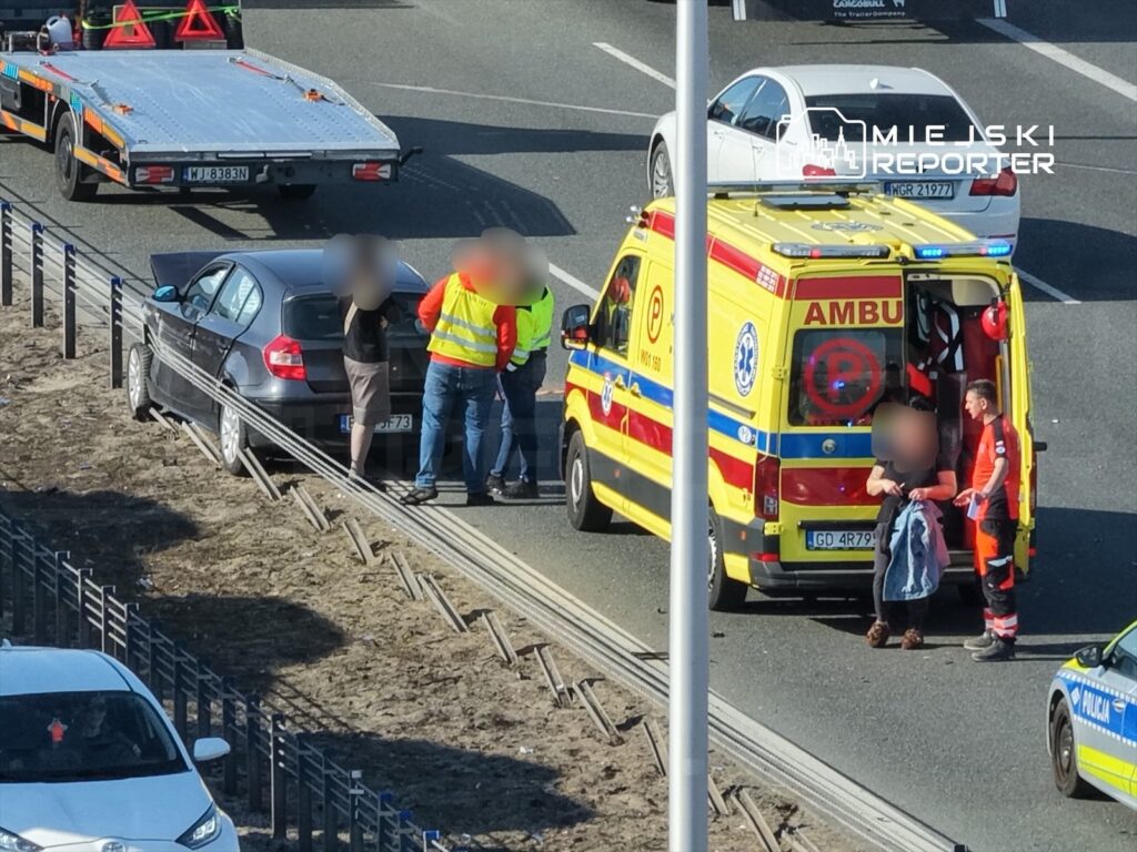 Kierowca samochodu osobowego rozmawia z ratownikami medycznymi obok karetki na drodze.