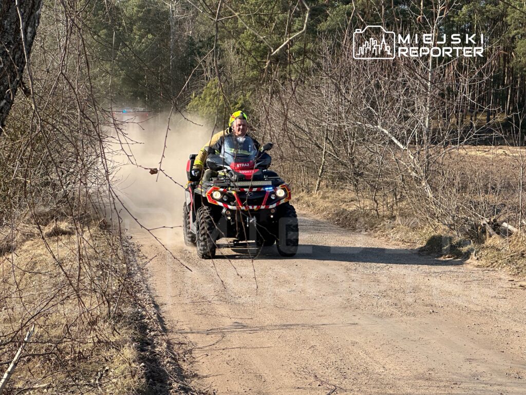 Mężczyzna w kasku jedzie na quadzie po piaszczystej drodze w lesie, w tle widoczne zarośla.