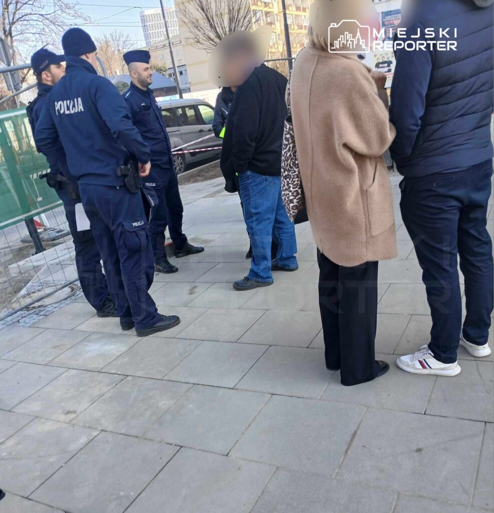 Grupa policjantów rozmawia z kilkoma osobami na chodniku w miejskim otoczeniu.