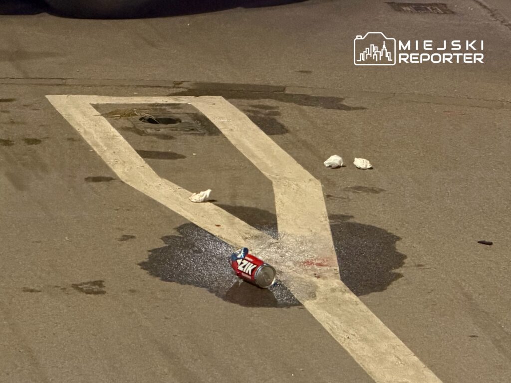 Pusta przestrzeń parkingowa z rozlaną cieczą, pustą puszką napoju i papierowymi odpadkami na asfalcie.
