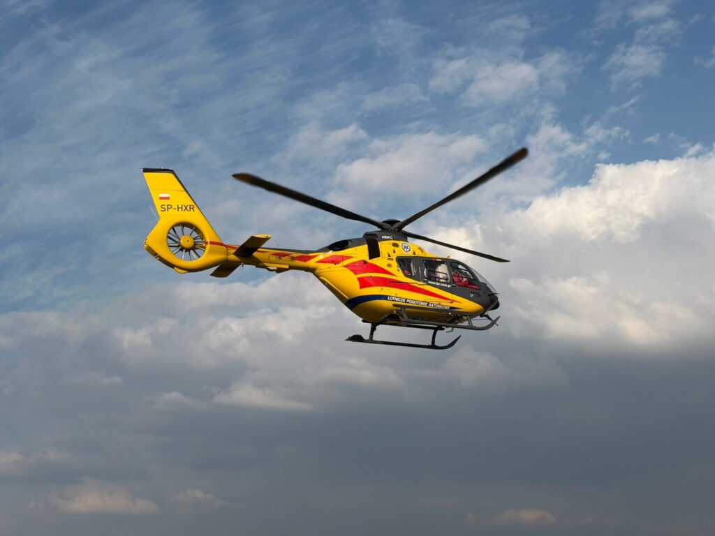 Żółty helikopter w powietrzu, przelatujący przez pochmurne niebo.