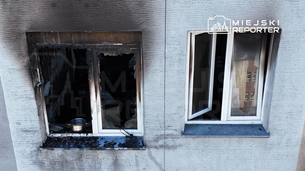 Spalone okna w budynku mieszkalnym, z widocznymi zniszczeniami i sadzą na elewacji.