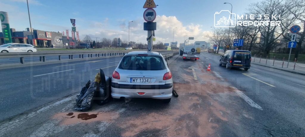Na jezdni stoi srebrny samochód osobowy obok worków z odpadami, a obok widać ślady płynnej substancji.