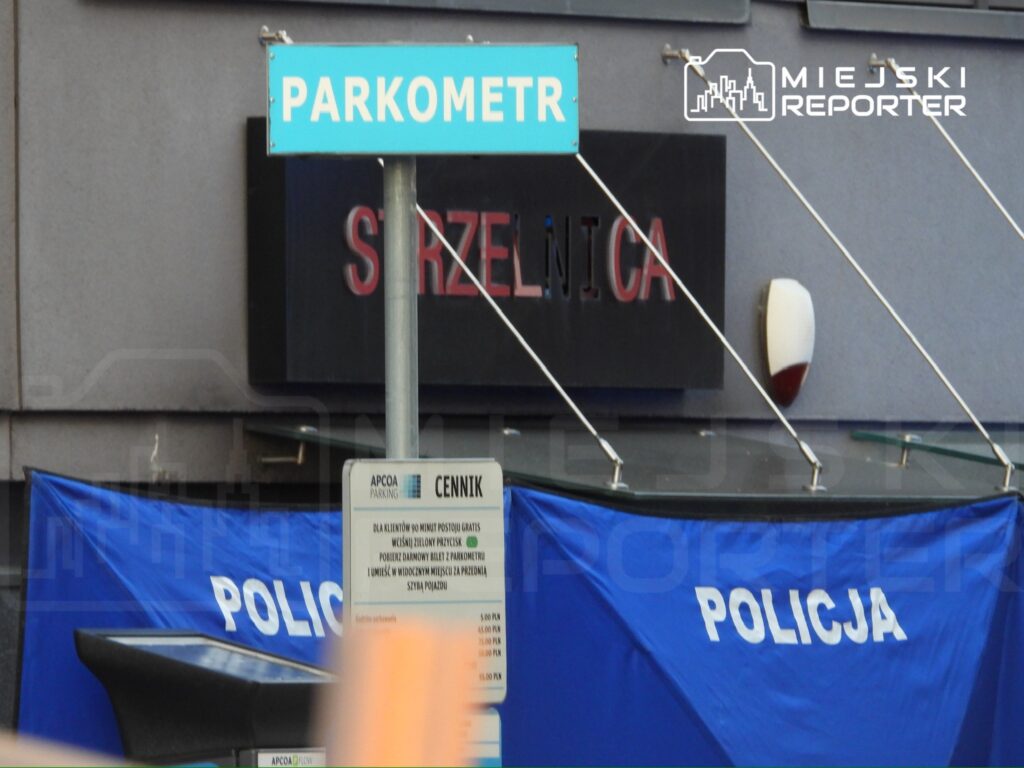 Znak "PARKOMETR" ustawiony obok niebieskiego namiotu z napisem "POLICJA" w miejskim otoczeniu.