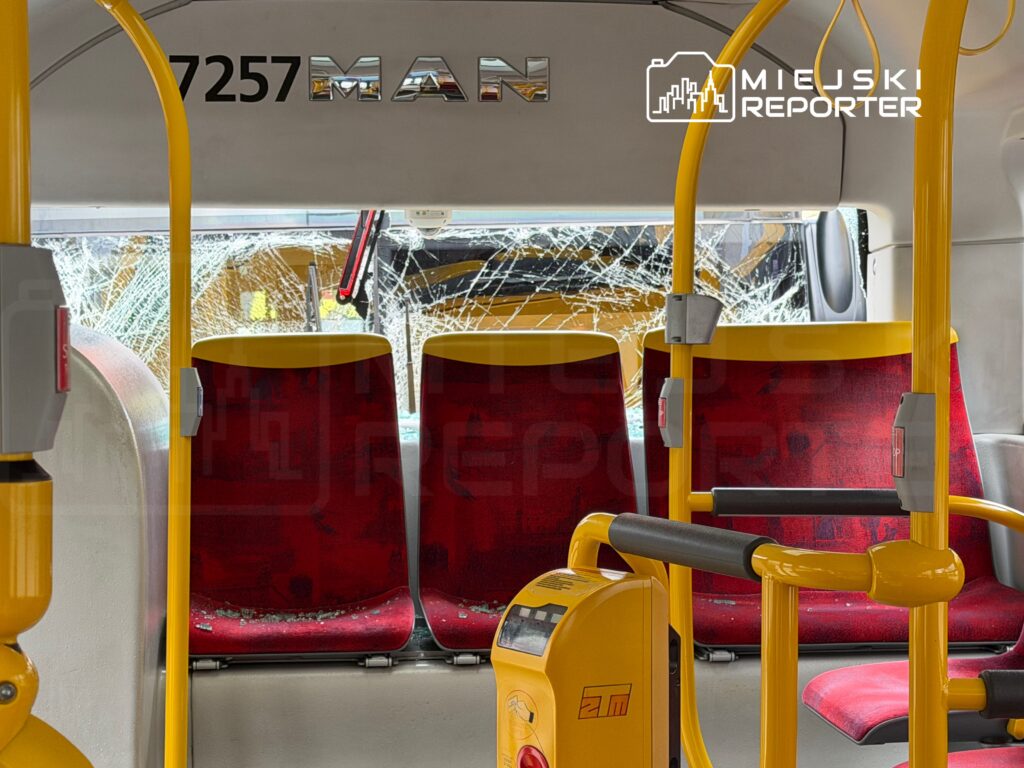 Wnętrze autobusu z uszkodzonymi siedzeniami i rozbitym tylnym oknem, na podłodze szkło.