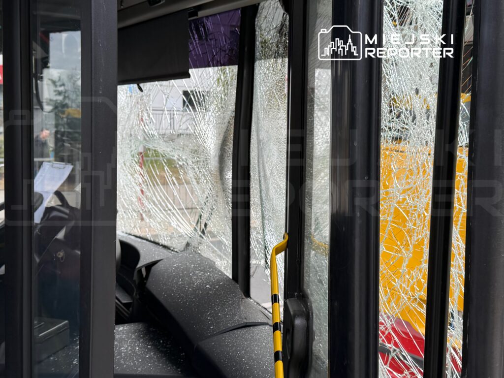 Zniszczona szyba w autobusie, z widocznymi pęknięciami i odłamkami szkła na siedzeniu obok.