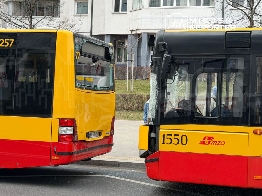 Dwa żółte autobusy komunikacji miejskiej stoją obok siebie, jeden z rozbitą szybą.