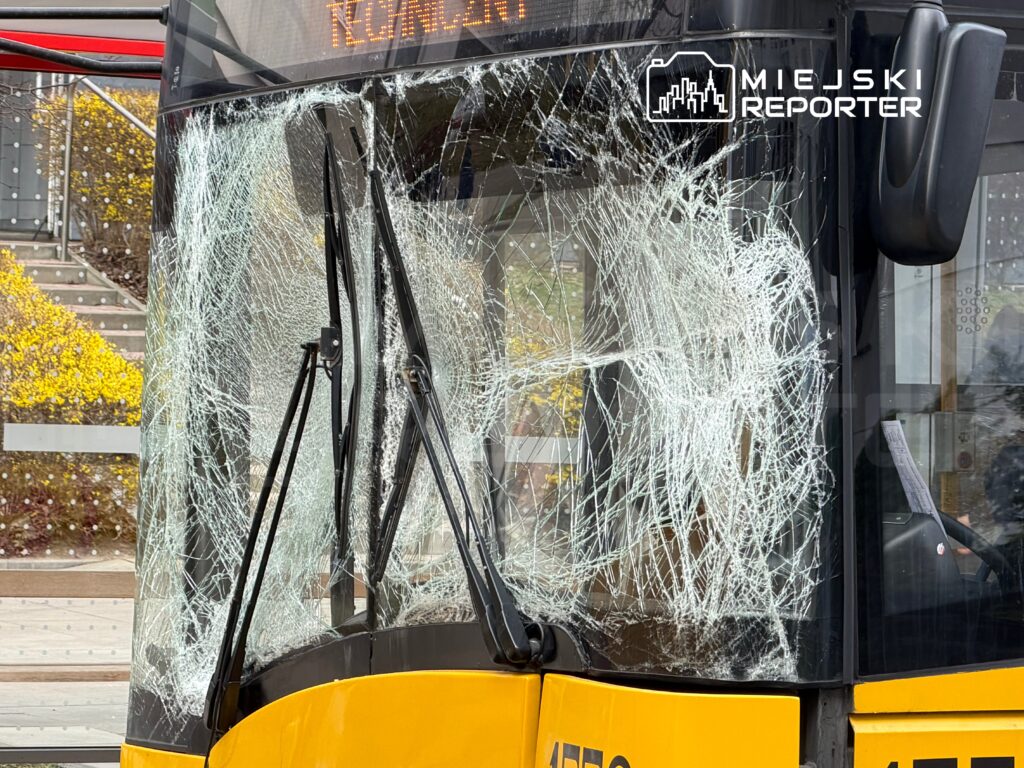 Witryna autobusu miejskiego z rozbitym szkłem, stojącego na przystanku w miejskim otoczeniu.