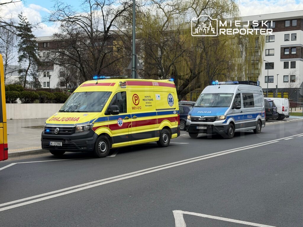 Karetka pogotowia i radiowóz policyjny zatrzymane na ulicy, obydwa z włączonymi sygnałami świetlnymi.