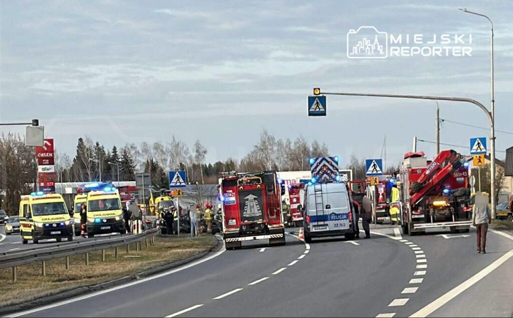 Na drodze znajdują się karetki pogotowia, pojazdy straży pożarnej oraz policja, prowadzące działania ratunkowe.
