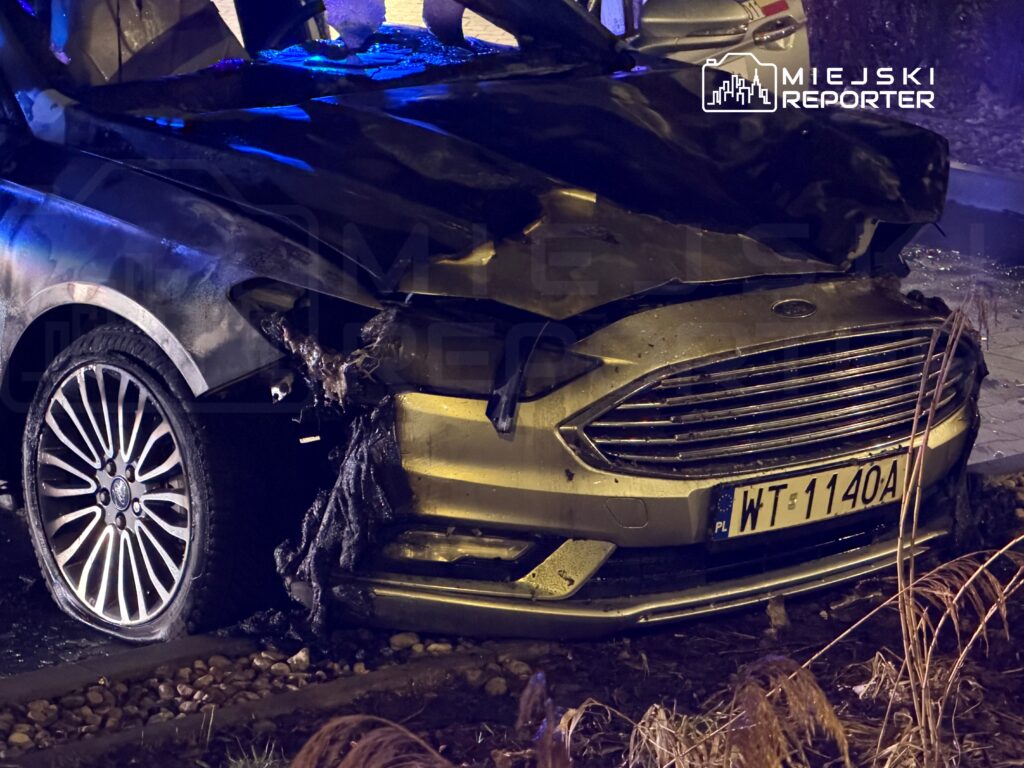 Spalony samochód osobowy stojący na poboczu drogi, z widocznymi uszkodzeniami przodu i opon.