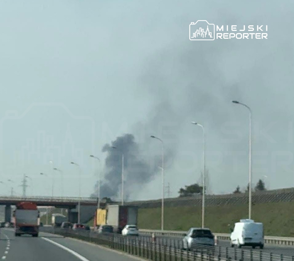 Czarny dym unoszący się w powietrzu z kierunku drogi, obok ruchu pojazdów na autostradzie.