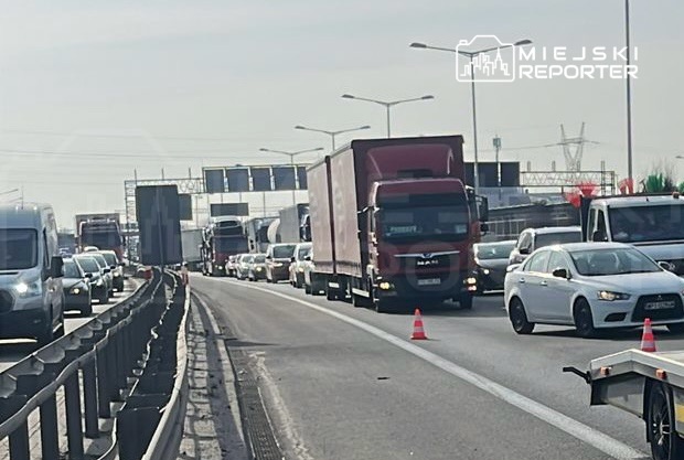 Zatory drogowe z ciężarówkami i samochodami osobowymi na autostradzie, w tle widoczne znaki drogowe.