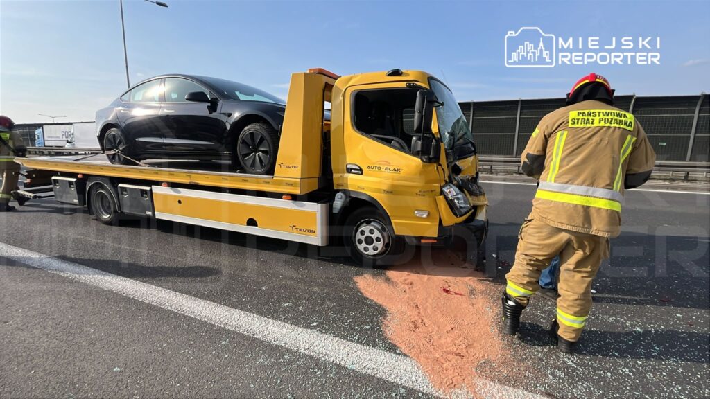 Na autostradzie strażak w mundurze zajmuje się usuwaniem uszkodzonego samochodu z lawety.