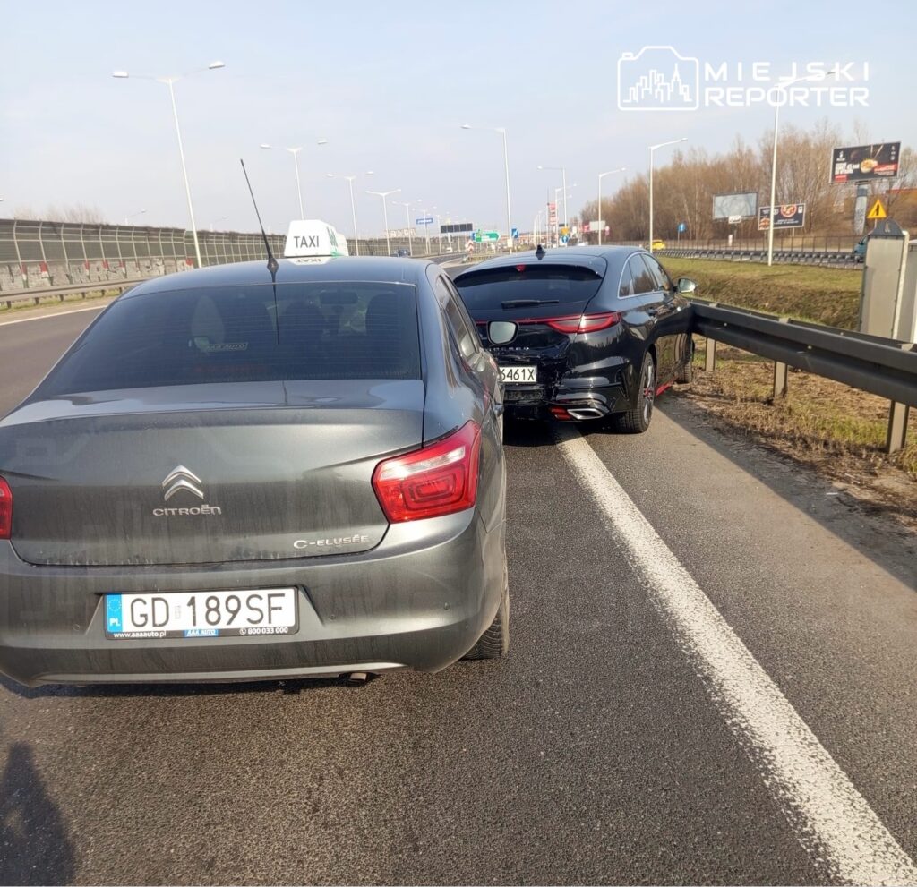 Dwa samochody osobowe zaparkowane na pasie ruchu, jeden z nich to taksówka z widocznym napisem na dachu.