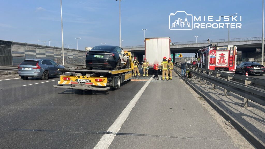 Grupa strażaków zabezpiecza miejsce zdarzenia drogowego na autostradzie, obok unieruchomionych pojazdów.