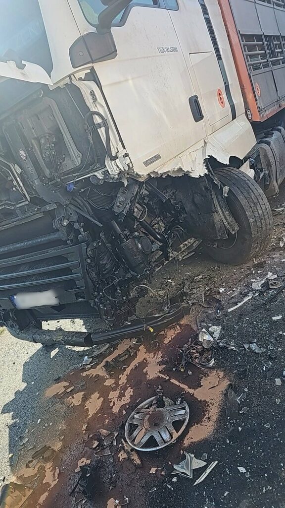 Uszkodzony ciężarowy pojazd leży na boku, w otoczeniu rozbitych elementów i plamy płynów eksploatacyjnych na drodze.