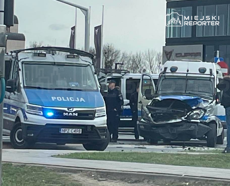 Policyjny van z uszkodzoną przednią częścią stoi na ulicy, obok niego funkcjonariusze interweniujący na miejscu zdarzenia.