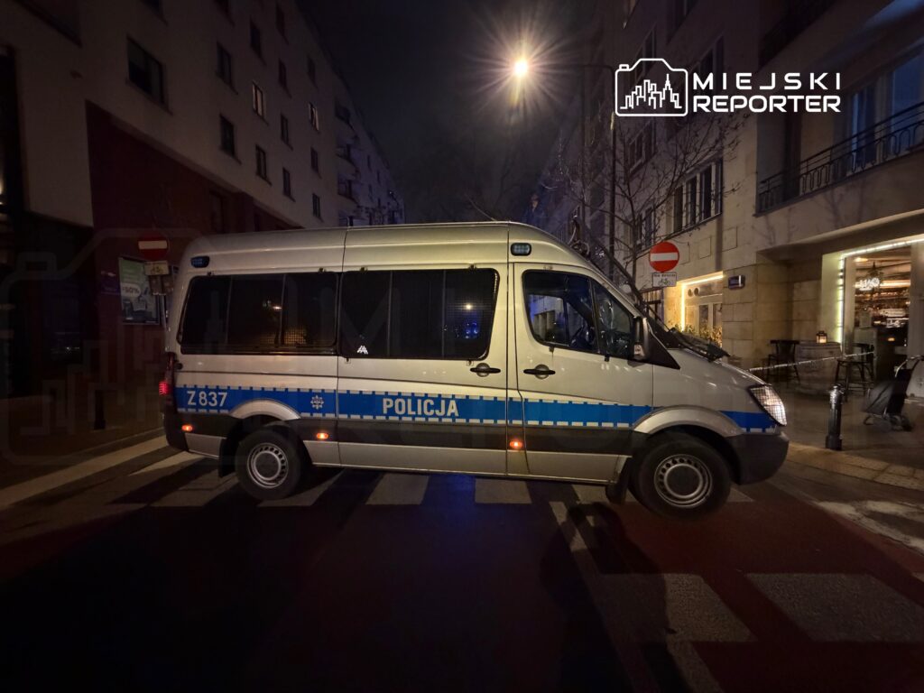 Policyjny radiowóz zaparkowany na ulicy w nocy, z widocznymi światłami i oznaczeniem "POLICJA".