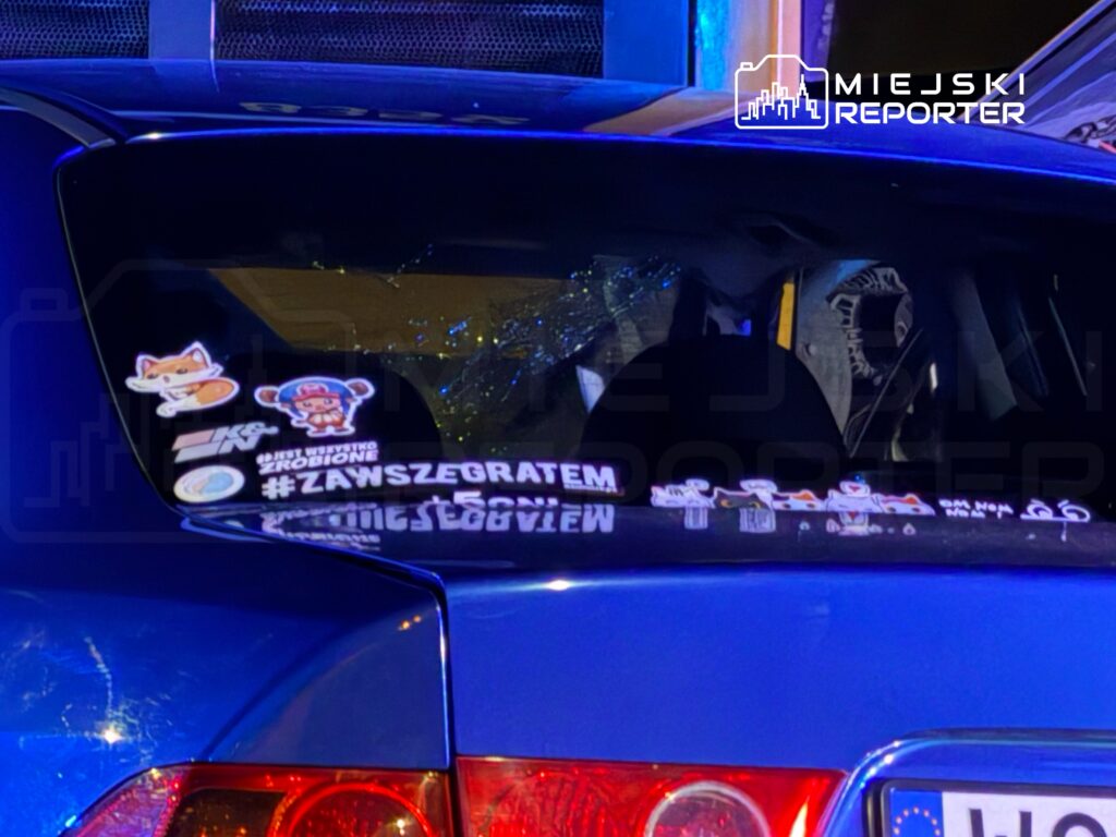 Na tylnej szybie niebieskiego samochodu umieszczone są różnorodne naklejki, w tym #ZAWSZEGRATEM oraz postacie z gier.