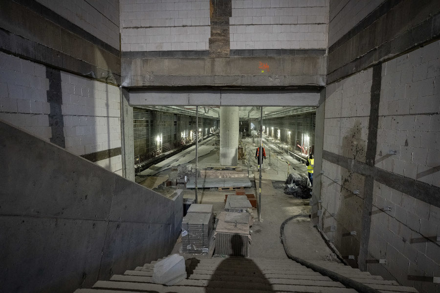 Klatka schodowa prowadząca do przestronnej budowy z widocznymi materiałami budowlanymi i oświetleniem roboczym.