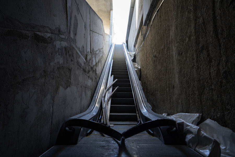Uszkodzona, nieczynną ruchoma schody prowadzące w górę w wąskim, betonowym tunelu z jasnym światłem na końcu.