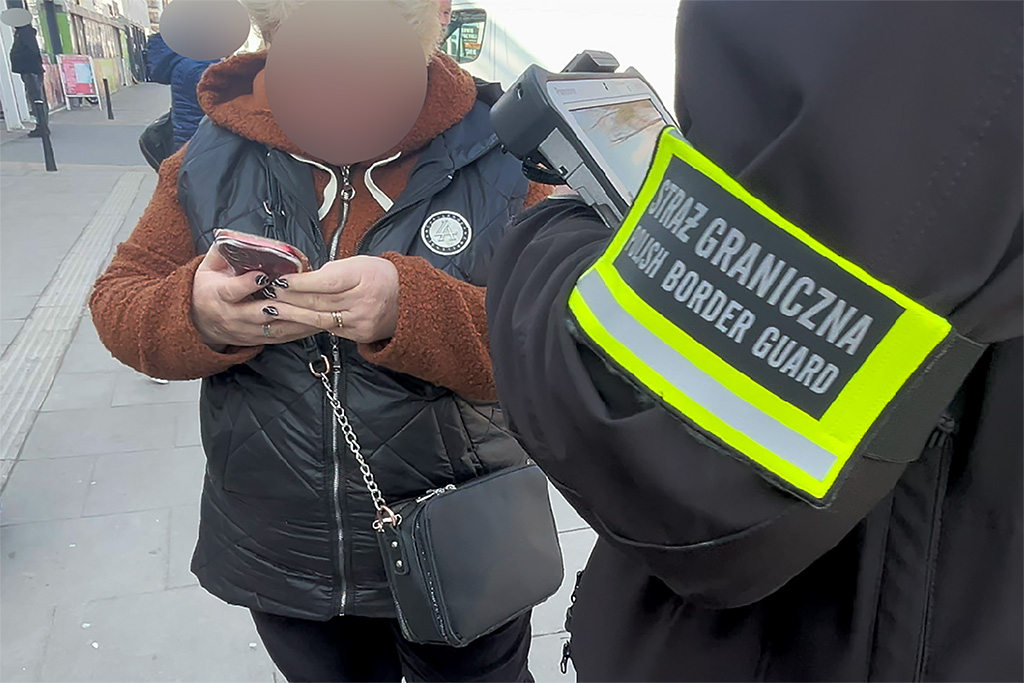 Kobieta w ciemnej kamizelce sprawdza telefon, obok niej funkcjonariusz Straży Granicznej z urządzeniem w ręku.