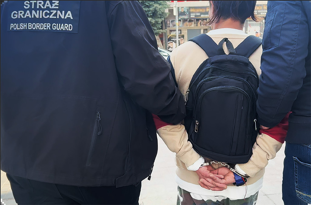 Mężczyzna z plecakiem unieruchomiony przez funkcjonariuszy Straży Granicznej na ulicy.