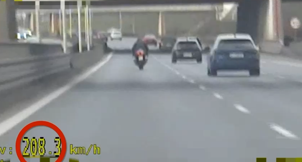 Motocyklista poruszający się z prędkością 208,3 km/h na ruchliwej drodze, mijający samochody osobowe.