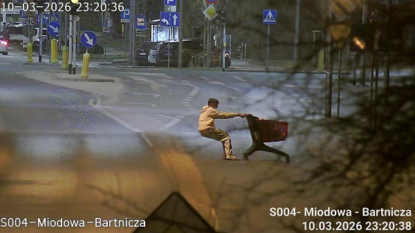 Dwaj mężczyźni szarpaną się w nocy na pustej ulicy, obok znaków drogowych i latarni.