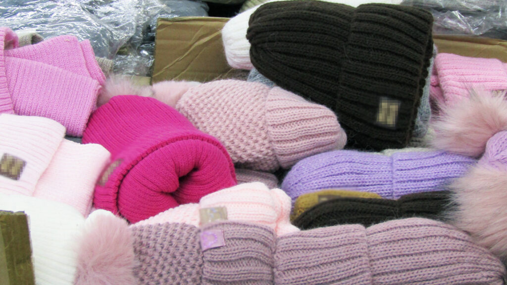 Kolorowe czapki z wełny w różnych odcieniach różu, fioletu i brązu ułożone w kartonie.