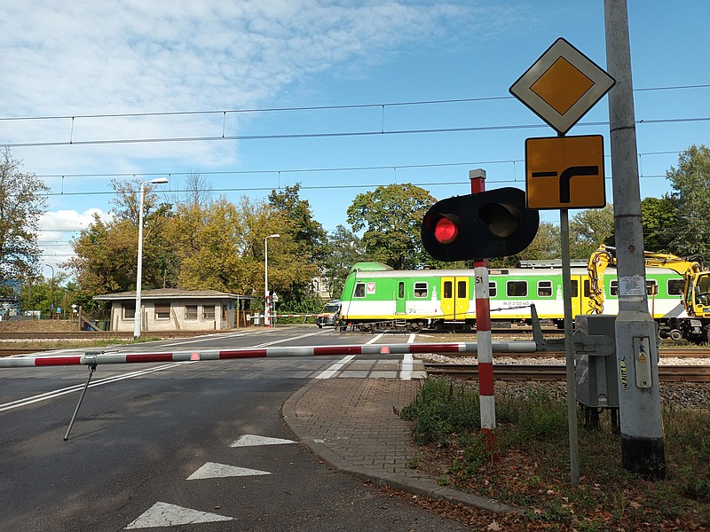 Zielony pociąg przejeżdża przez przejazd kolejowy, a czerwone światło sygnalizacji wskazuje na zakaz wjazdu.