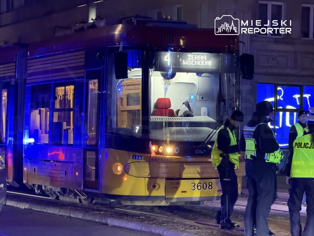 Tramwaj z numerem 4 zatrzymany na przystanku, obok grupy policjantów w kamizelkach odblaskowych.