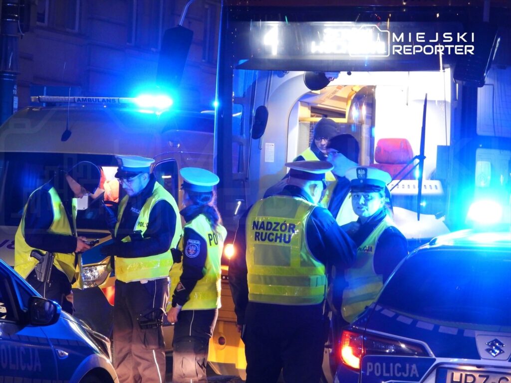 Grupa policjantów w odblaskowych kamizelkach prowadzi interwencję nocą przy oświetlonym autobusie.