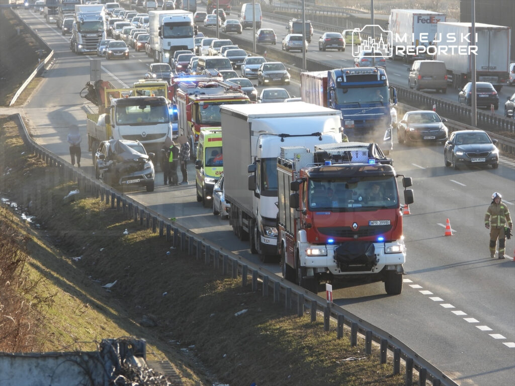 Wielu ratowników medycznych i strażaków przy samochodzie osobowym po wypadku na ruchliwej drodze.